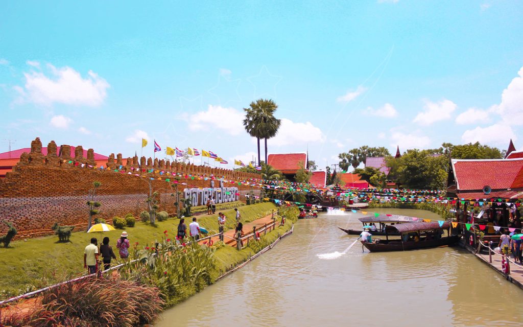Bateaux à longue queue sur un canal près d'un mur de brique et de fanions colorés, marché flottant thaï et touristes