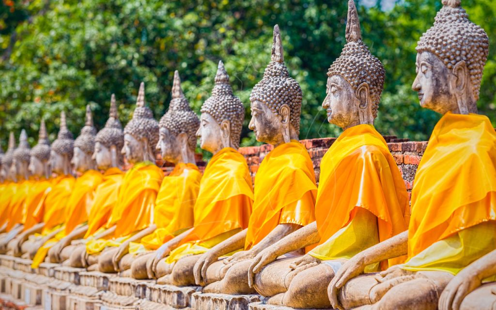 Rangée de statues de Bouddha assises en pierre drapées de robes safran orange dans un temple d'Ayutthaya, Thaïlande