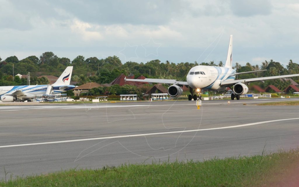Jet di Bangkok Airways in rullaggio sulla pista di un aeroporto tropicale con palme ed edifici del terminal dai tetti di paglia