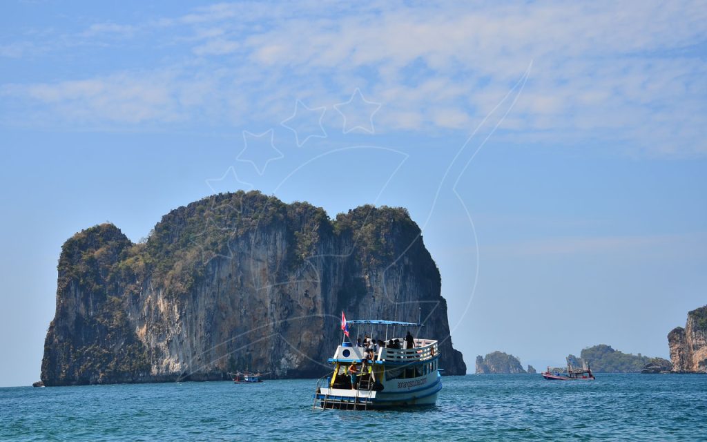 载着游客的木质潜水船停泊在平静碧蓝海面上高耸的石灰岩喀斯特岛屿旁