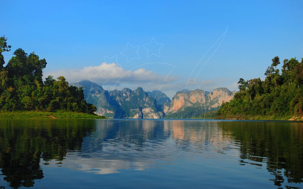 Lac émeraude calme reflétant des falaises karstiques calcaires et des rives couvertes de jungle sous un ciel bleu limpide