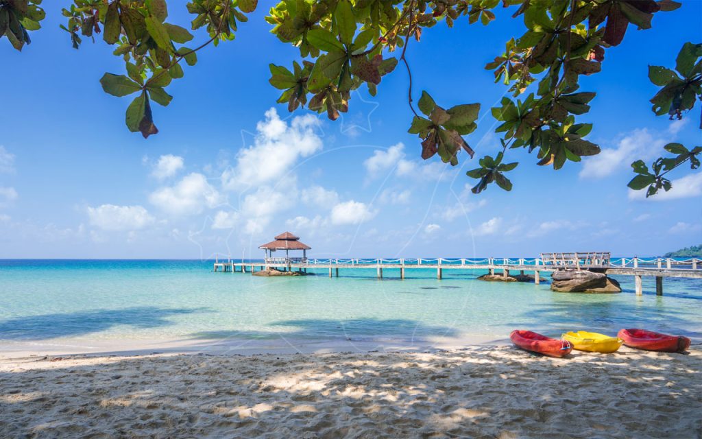 Holzpier mit rot gedecktem Pavillon über türkisfarbenem Wasser, drei Kajaks am weißen Sandstrand, von Blättern umrahmt