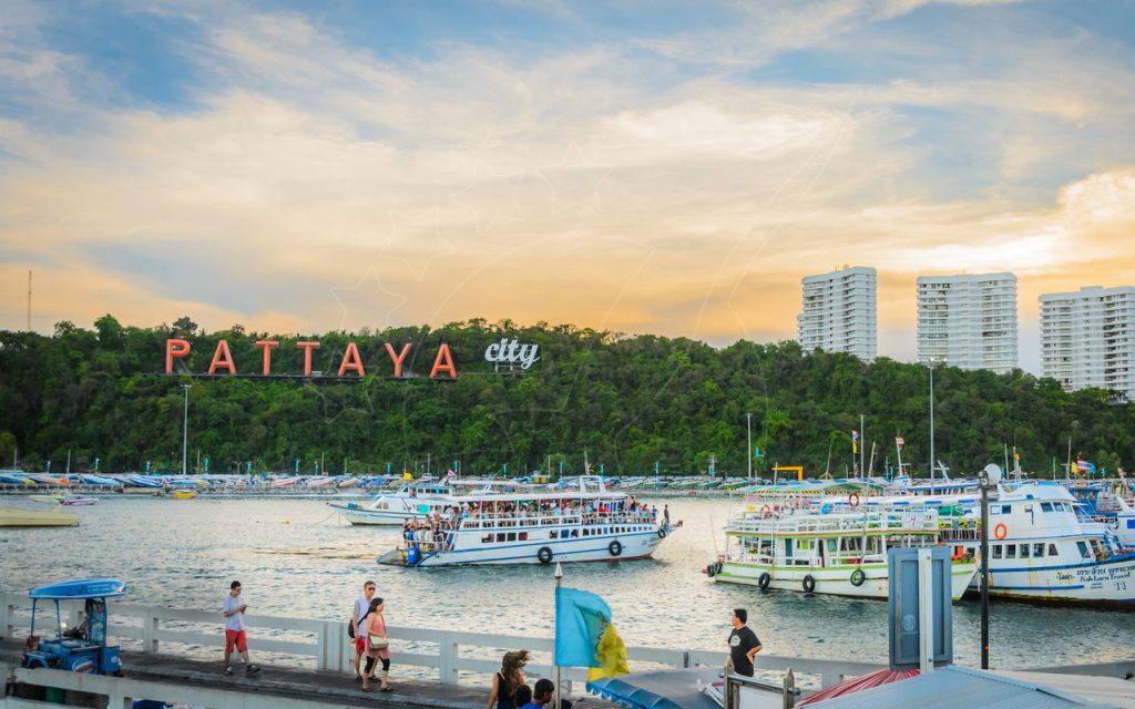 عبّارات ركاب في رصيف بالي هاي في باتايا مع لافتة PATTAYA على التل وسياح وأبراج سكنية عند الغروب