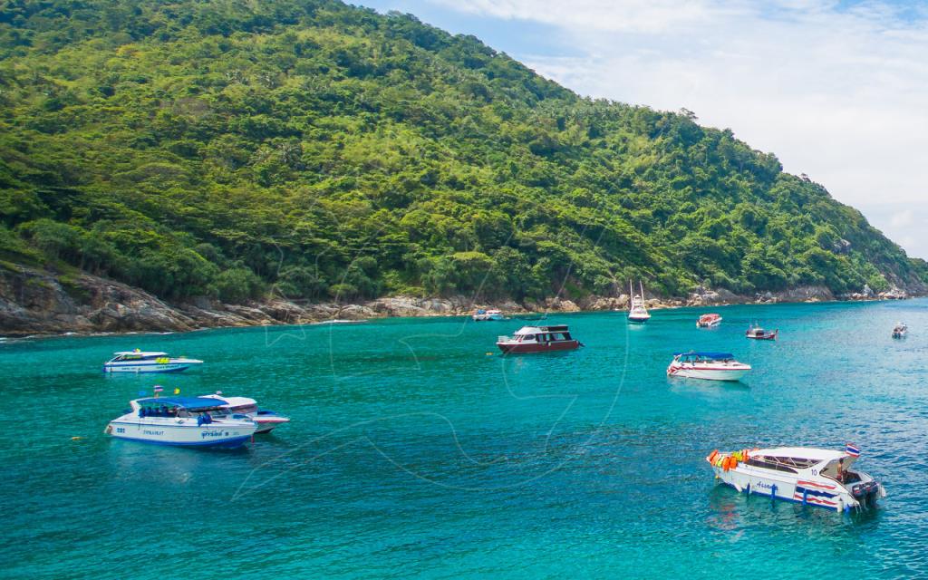 Bateaux rapides et long-tail boats au mouillage dans une baie turquoise sous un promontoire verdoyant, Thaïlande