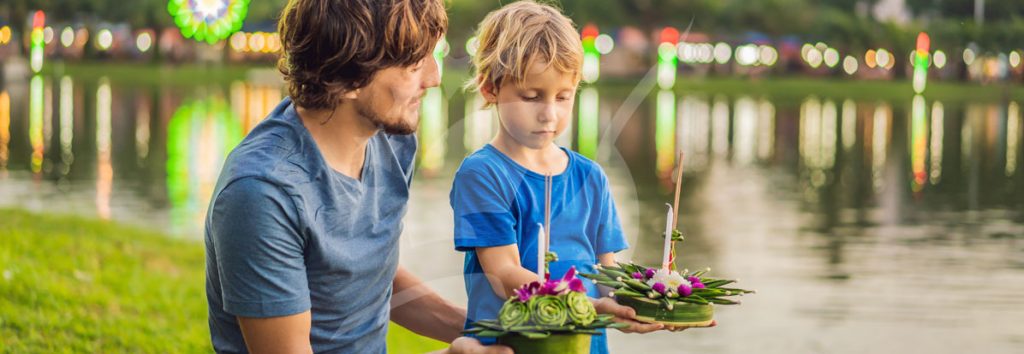 Un adulte et un enfant déposent des couronnes de fleurs dans l'eau depuis un ponton au crépuscule