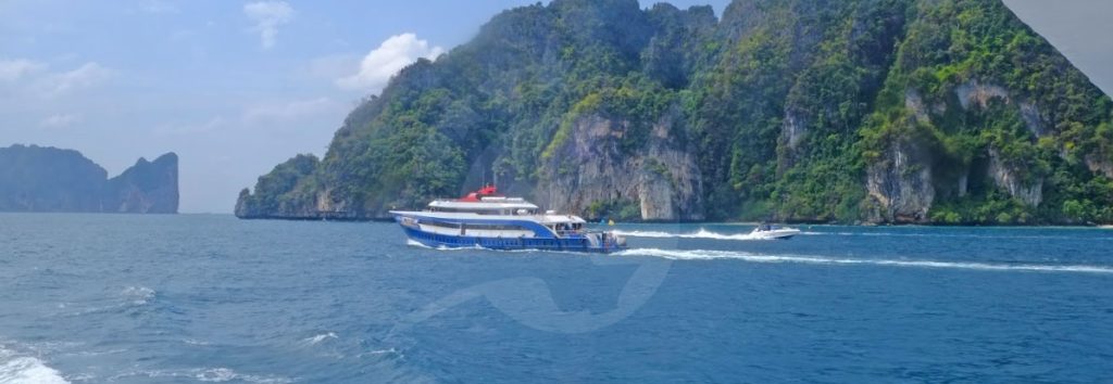 Traghetto blu e rosso in navigazione davanti a scogliere calcaree in acque tropicali