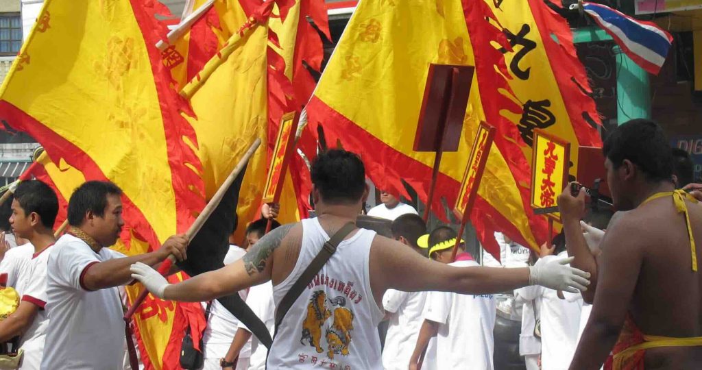 Foule portant des drapeaux jaunes et rouges avec des caractères chinois lors d'une procession de rue en Thaïlande