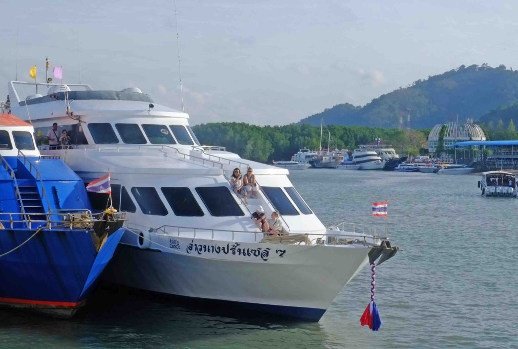 Weiß-blaue Passagierfähre am Pier mit einsteigenden Touristen, bergige Küste im Hintergrund
