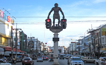 Bronze sculpture of man standing on globe mounted on urban street pole amid traffic